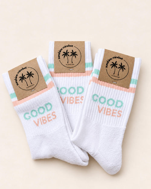 Drei Paar weiße Good Vibes Socken mit türkisen und hellorangen Streifen und sunshine mindset Papierbanderole.